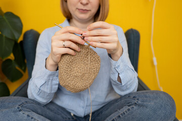 Anonymous young woman crocheting while sitting at home in an armchair. Close-up of yarn and hook.