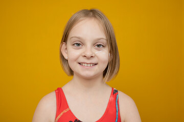 A girl in a red swimsuit with cream on her face on a yellow background.