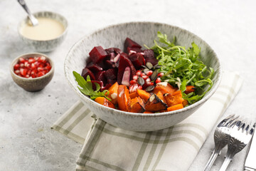 A grey deep bowl with warm winter autumn salad with arugula, red beetroot, baked pumpkin and hummus dressing cubes on a grey background