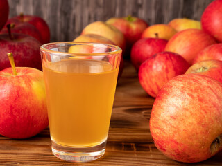Apple cider vinegar in a glass with apples on a wooden background.