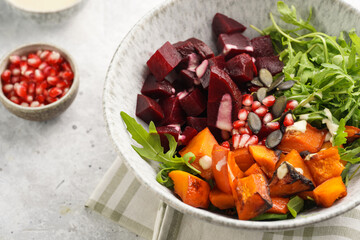 A grey deep bowl with warm winter autumn salad with arugula, red beetroot, baked pumpkin and hummus...