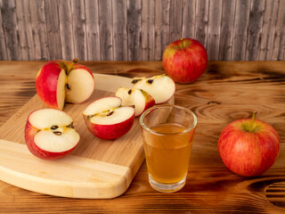 Apple cider vinegar in a glass with apples on a wooden background.