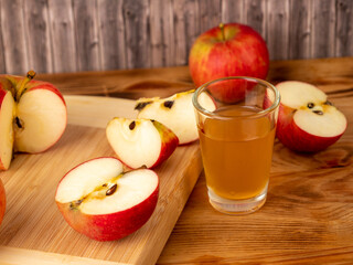 Apple cider vinegar in a glass with apples on a wooden background.