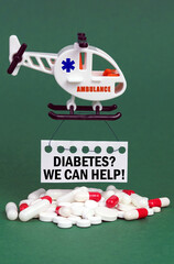 On a green surface, an ambulance helicopter, pills and a white sign with the inscription - Diabetes We Can Help