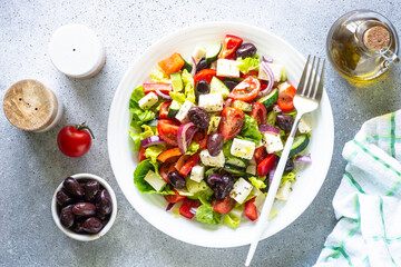 Greek salad with olives, feta cheese and fresh vegetables. Top view on light stone table.