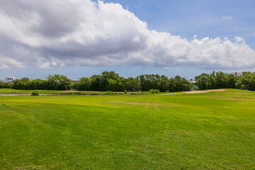 Beautiful landscape view of green grass golf field on green trees and blue sky with white clouds background. Aruba. 