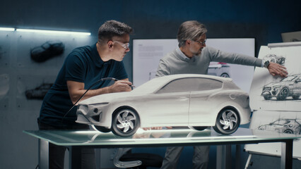 Two experienced automotive engineers discuss the car design looking at the sketches on the board....