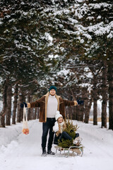 Fototapeta na wymiar A couple having fun with sleigh in a Christmas tree forest , eating mandarins and enjoying a snowy day. a wonderful couple falling in love in a winter fairytale, getting ready for winter holidays. 