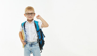 Back to school. Funny little boy from elementary school with a book, a backpack and glasses on a white background. Laughs merrily. Preparation for school. Concept of early development