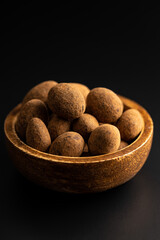 Almonds in chocolate coated in cocoa in bowl on dark table.