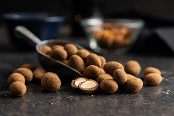 Almonds in chocolate coated in cocoa in scoop on dark table.
