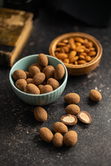 Almonds in chocolate coated in cocoa in bowl on dark table.