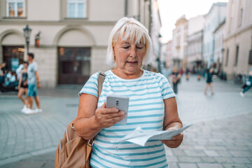Mature traveller woman walking on old town holding tourist map and phone at Krakow, Poland. Travel and active lifestyle concept. 