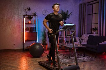 Fototapeta na wymiar Attractive young sports asian man doing fitness exercise, running on treadmill . Athletic and muscular male having actively workout indoor, at modern apartment at night time at home.