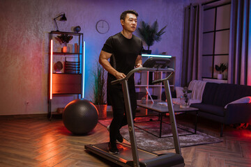 Fototapeta na wymiar Attractive young sports asian man doing fitness exercise, running on treadmill . Athletic and muscular male having actively workout indoor, at modern apartment at night time at home.