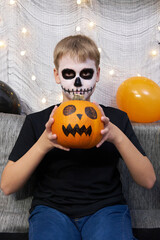 Scary child with a make-up in form of a skeleton and with a pumpkin in his hands