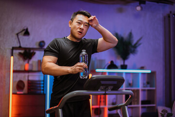Portrait of handsome active thirsty and dynamic young asian man doing sport fitness at home running...