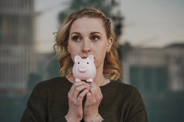 blond young negative thinking woman with depressed look holding pink piggy bank infront of her head...