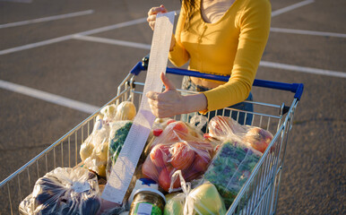 Young woman with shopping cart full of fresh and healthy food on the parking place near the supermarket