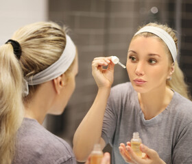 woman looking in the mirror in the bathroom and taking care of her skin.