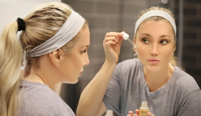 woman looking in the mirror in the bathroom and taking care of her skin.