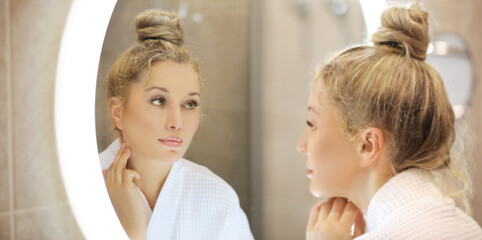 woman looking in the mirror in the bathroom and taking care of her skin.