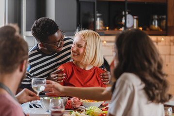 Young diverse people having a holiday party at home, preparing food, drinking, talking, and enjoying