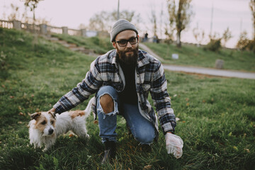 A man cleans up poop after his dog while walking on the lawn.