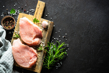 Turkey steaks or fillet with spices and herbs at wooden cutting board at black stone table. Top view with copy space.