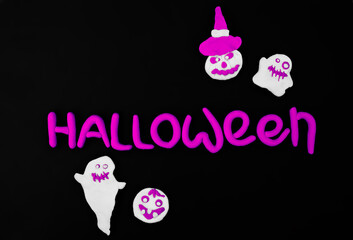 halloween lilac inscription text with white ghosts and scary pumpkins from air plasticine on black background