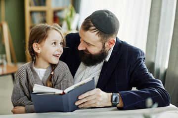 Portrait of smiling jewish father reading book with daughter at home