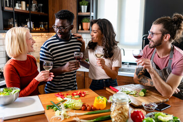 Young diverse people having a holiday party at home, preparing food, drinking, talking, and enjoying