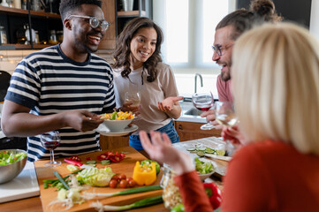 Young diverse people having a holiday party at home, preparing food, drinking, talking, and enjoying