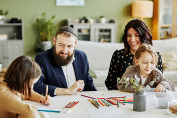 Portrait of modern jewish family drawing together while sitting at table , focus on smiling father...