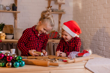 boy and girl in red christmas pajamas prepare a gingerbread house and decorate it with icing at home