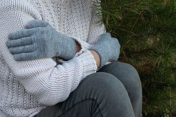 A woman in a knitted white sweater and gloves hugging herself trying to keep warm. Energy crisis