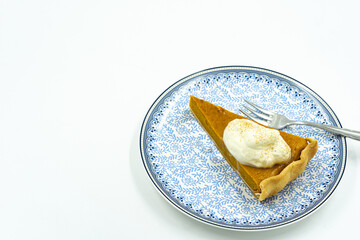 Isolated piece of orange pumpkin pie with whipped cream on plate.