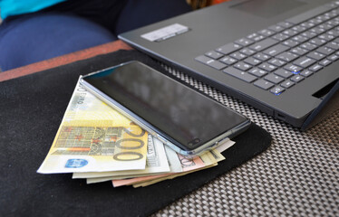 a pack of euro bills and a smartphone near the laptop keyboard. preparation for making purchases via the Internet and counting cash to replenish the card