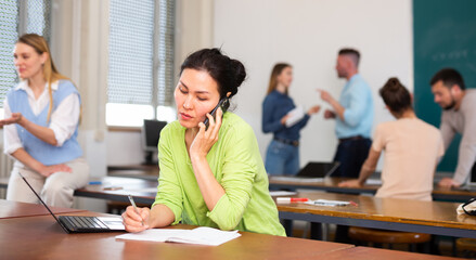 Asian girl student studying in a university auditorium during a break after classes is discussing something important on a ..mobile phone