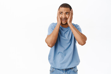 Fototapeta premium Portrait of scared and worried arab man, holds hands on head and looking in panic at camera, standing over white background