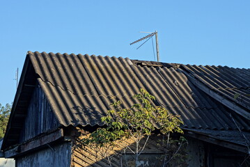 green wooden attic of a old rural house under a gray slate roof against a blue sky