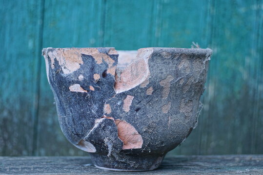 One Old Black Large Dirty Broken Ceramic Pot With A Crack Stands On A Gray Table Against A Green Wall