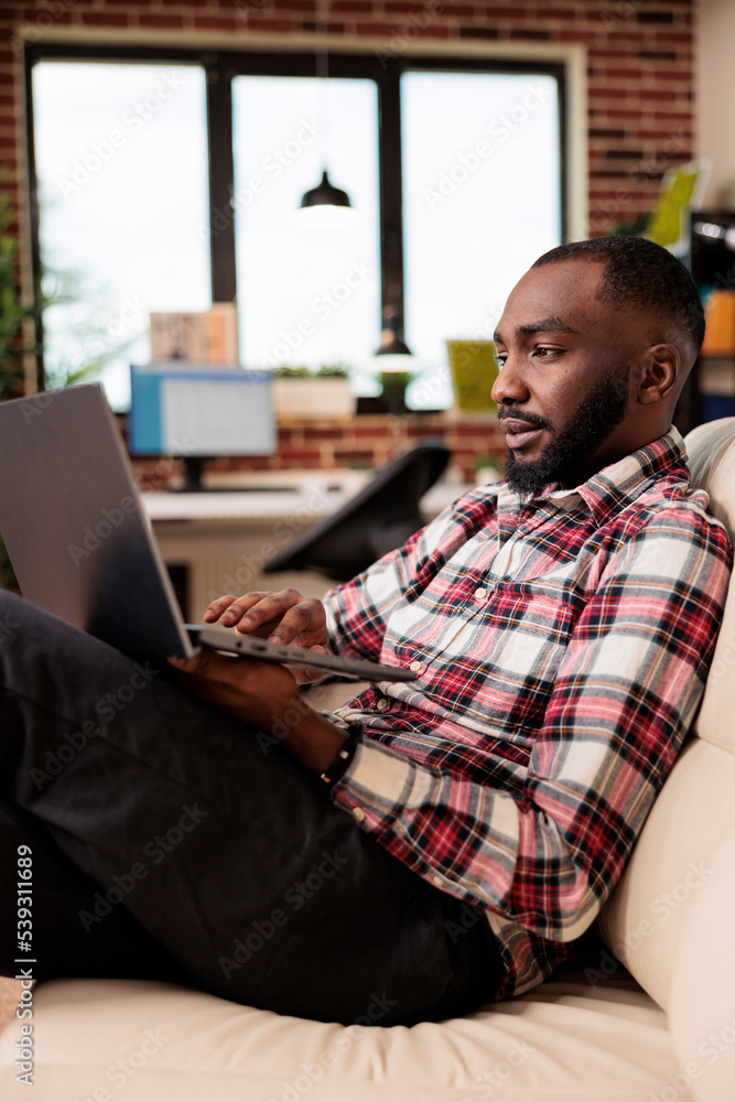 Poster office employee working on laptop at home, doing remote job and sitting on couch. person using compu