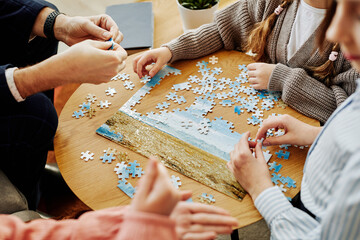 Close up of unrecognizable family playing jigsaw puzzle game together at home - obrazy, fototapety, plakaty