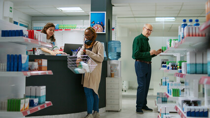 Obraz premium Young customer taking boxes of pills from pharmacy shelves to buy prescription treatment, buying pharmaceutics and packages of medicaments. Asking pharmacist about vitamins. Tripod shot.