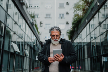 Portrait of a senior businessman using tablet outside of the office building