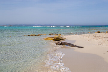 Rocky beach with a turquoise blue sea and a piece of wooden and waves in spain