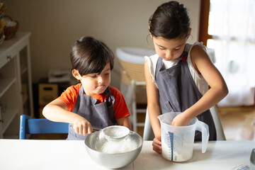 two children wearing grey aprons sifting flour