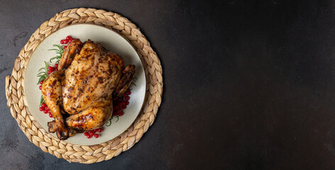 Roasted chicken for festive dinner. Cooked chicken or turkey with herb rosemary and berries on dark table. Thanksgiving holiday concept. Banner format, copy space