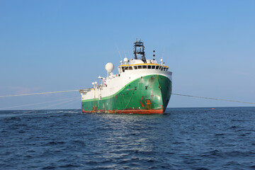 Seismic survey vessel moving ahead with all towed in sea equipment deployed. Oil and gas exploration. Restricted manoeuvrability day signals hoisted. Front view.